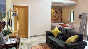 Een gezellige kamer met een houten trap, een zwarte bank met gele kussens, een vloerkleed met dessin en een bed met bloemenbeddengoed.