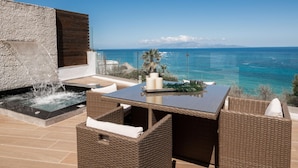 A balcony with a hot tub, wicker furniture, and a view of the ocean.