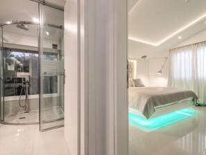 A modern hotel room with a glass shower enclosure, a bed with a light-up underlay, and a minimalist design.