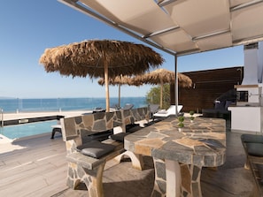 An outdoor seating area with stone tables and benches, a pool, and a view of the sea.