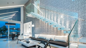 A modern living room with a glass staircase, a sofa, and a dining area.