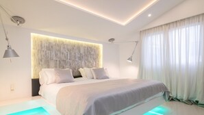 A modern bedroom with a large bed, recessed ceiling lighting, and a built-in headboard.