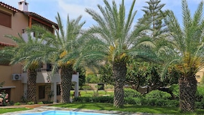 A swimming pool surrounded by palm trees and a building with a tiled roof. - Fantastic Holiday Home in Karteros With Pool (Hersonissos)
