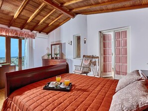 A bedroom with a large bed, a wooden headboard, a dresser, a chair, a window with curtains, and a door with a pink panel.