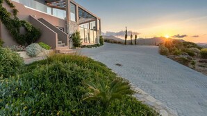 Uma casa moderna com um caminho de entrada pavimentado, uma pérgula e um jardim com diversas plantas e flores.