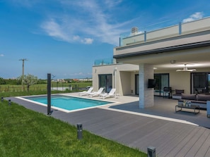 Ett modernt hus med en swimmingpool, utomhusmöbler och en stor balkong med glasväggar.