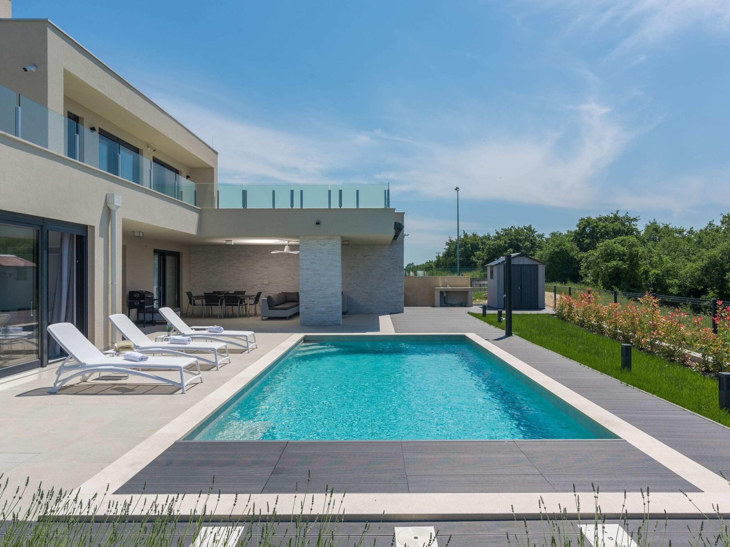 A modern outdoor swimming pool with lounge chairs, a covered seating area, and a small shed.