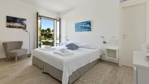 A modern bedroom with a bed, a chair, a desk, and a view of greenery outside. - 661 Villa con Piscina e Vista Panoramica a Ostuni (Ostuni)