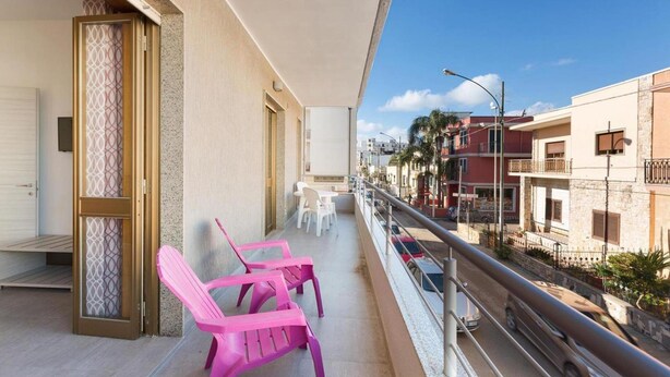 Un balcón con sillas rosadas, una mesa y vistas a una calle con edificios.