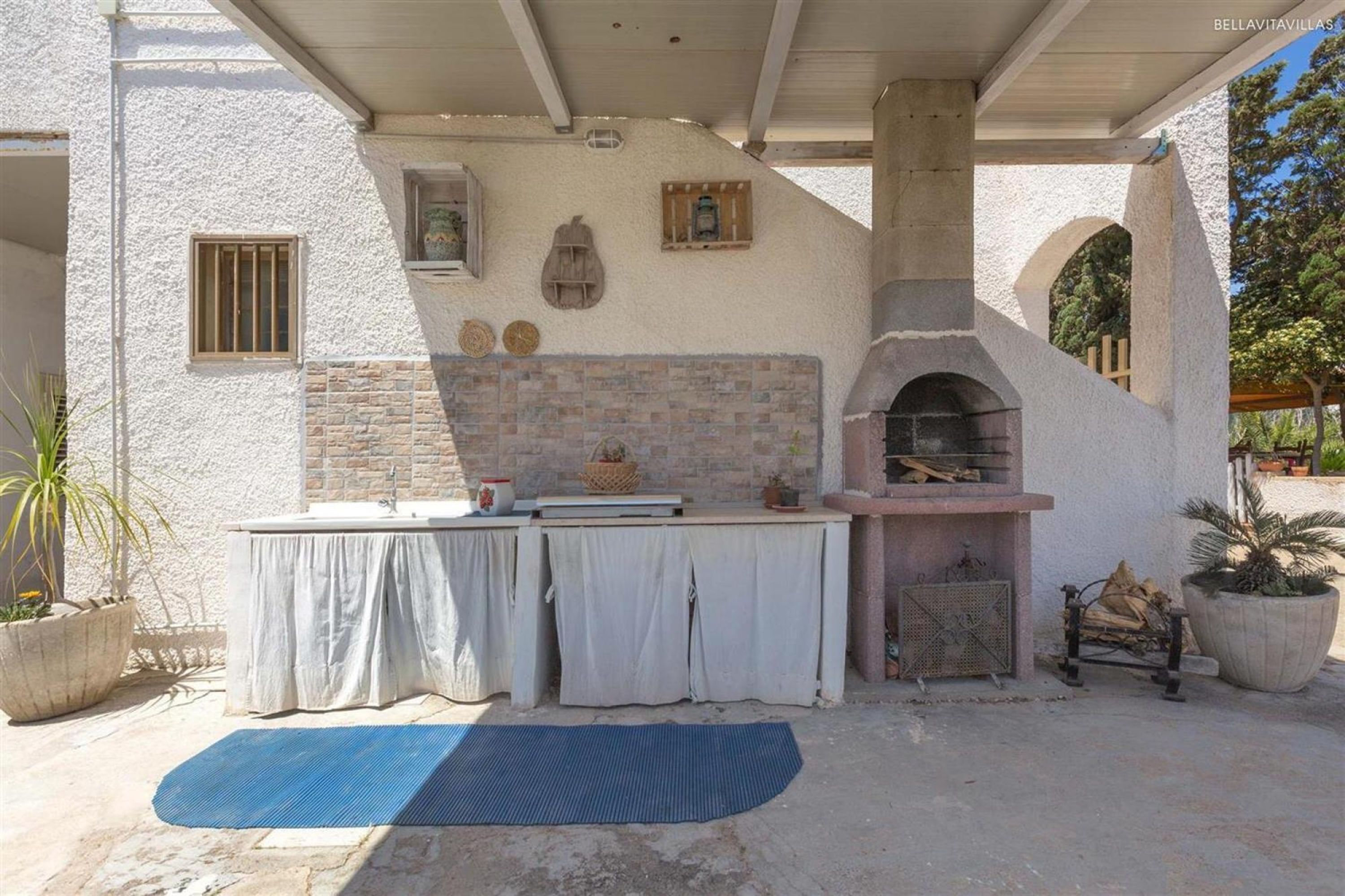 An outdoor kitchen area with a brick oven, a table with a white tablecloth, and potted plants.