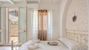 A bedroom with a bed, a wall-mounted light fixture, and a door leading to a balcony. - 1642 Tenuta Fioravante - Mono Afrodite (Porto Cesareo)