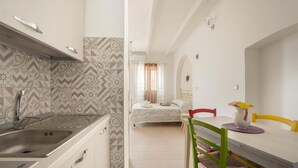 A kitchen with a modern design, a dining area with a table and chairs, and a bedroom with a bed and curtains. - 1642 Tenuta Fioravante - Mono Afrodite (Porto Cesareo)