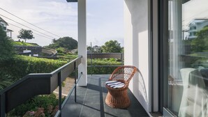 Ein Balkon mit Korbstuhl, Glastür und Blick auf eine grüne Landschaft.