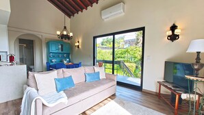Ein Wohnzimmer mit einem beigen Sofa, einem Fernseher und einem Essbereich mit einem blauen Tisch und Stühlen.