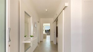 A hallway with a door on the left, a mirror, and a plant on the wall. - 1934 Villa Punta Ristola (Castrignano del Capo)
