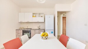 Una cocina moderna con armarios blancos, un refrigerador blanco y una mesa de comedor con un tazón de fruta.