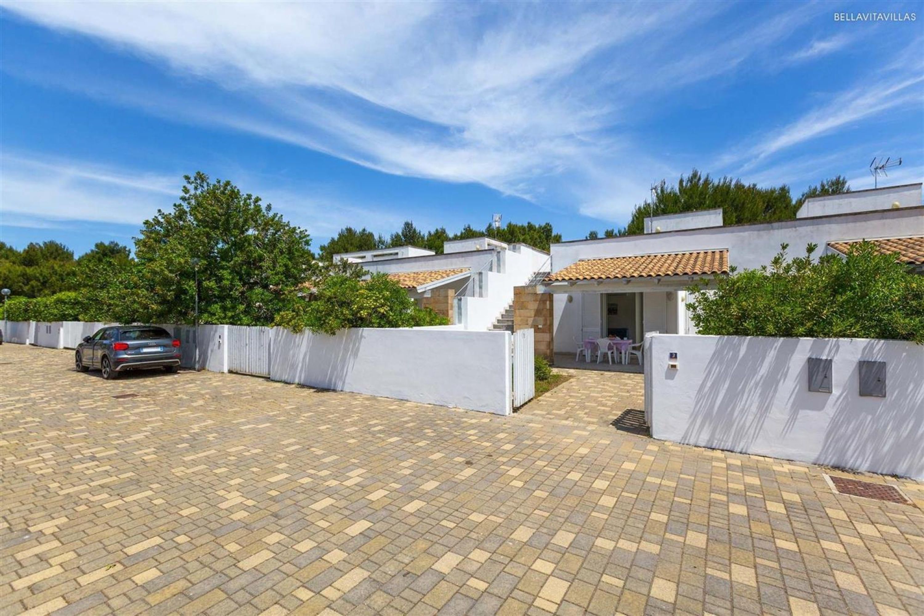 A modern villa with a paved driveway, a car parked on the left, and a white fence surrounding the property.