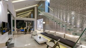 Moderni sisustus, jossa on lasista tehty portaikko, oleskelualue sohvineen ja tuoleineen sekä ruokailutila pöytineen ja tuoleineen.