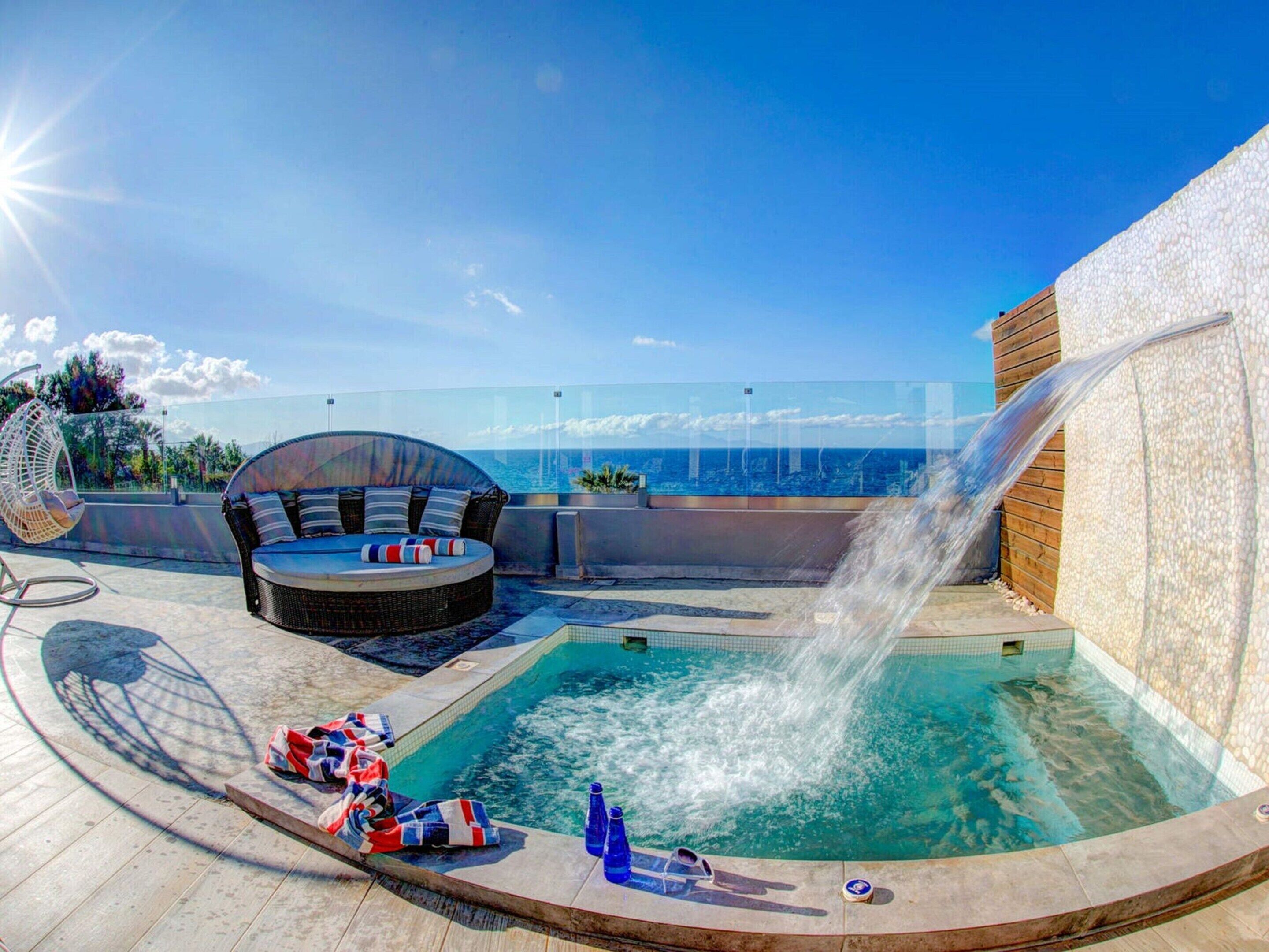 A rooftop pool with a hot tub and seating area, overlooking the ocean.