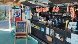 A rustic outdoor bar with a chalkboard menu, a Pepsi refrigerator, and various snacks hanging above the counter. - Apartment in Mpenitses With Sea Views & Pool (Corfu)