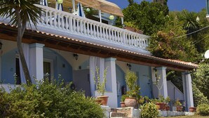 A two-story building with a balcony, potted plants, and a clear blue sky. - Apartment in Mpenitses With Sea Views & Pool (Corfu)