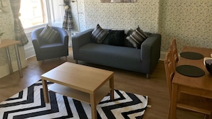 A living room with a grey sofa, two armchairs, a wooden coffee table, and a dining table with chairs. There is a patterned wallpaper and a framed picture on the wall. - Stunning 3-bed Apartment in Edinburgh (Edinburgh)