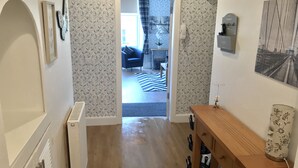 A hallway with patterned wallpaper, a wooden bench, and a door leading to a living area with a sofa and a striped rug. - Stunning 3-bed Apartment in Edinburgh (Edinburgh)
