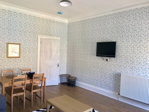 A room with a wooden dining table, chairs, a TV mounted on the wall, a white door, and patterned wallpaper. - Stunning 3-bed Apartment in Edinburgh (Edinburgh)