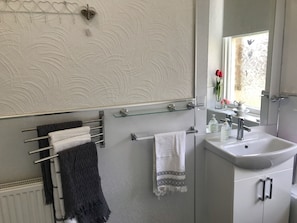 A bathroom with a towel rack, glass shelf, sink, and a window with flowers. - Stunning 3-bed Apartment in Edinburgh (Edinburgh)