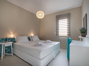 A bedroom with a large bed, bedside tables, a hanging light fixture, a window with blinds, and a potted plant on a side table. - Modern Villa With Private Pool in Plakias (Agios Vasileios)