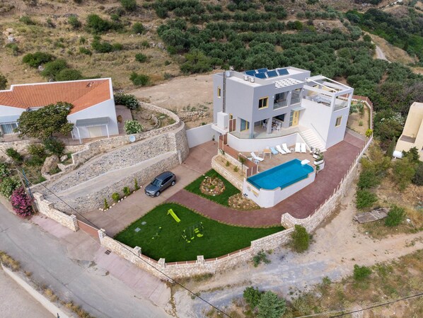 Una casa moderna de dos pisos con piscina, un muro de piedra y un coche estacionado en la entrada.
