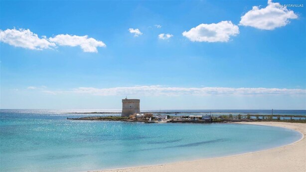 Une plage avec un phare, un ciel bleu dégagé et une mer calme.