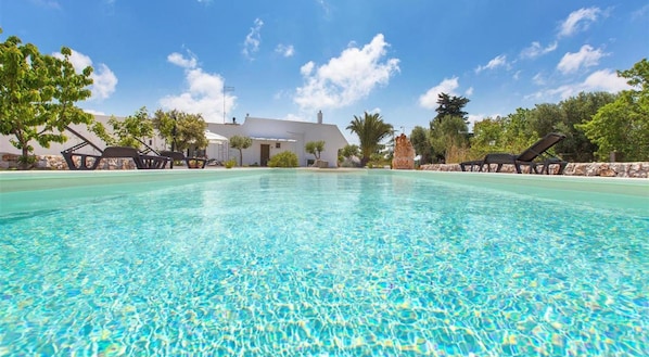 A clear swimming pool with lounge chairs and a white building in the background.