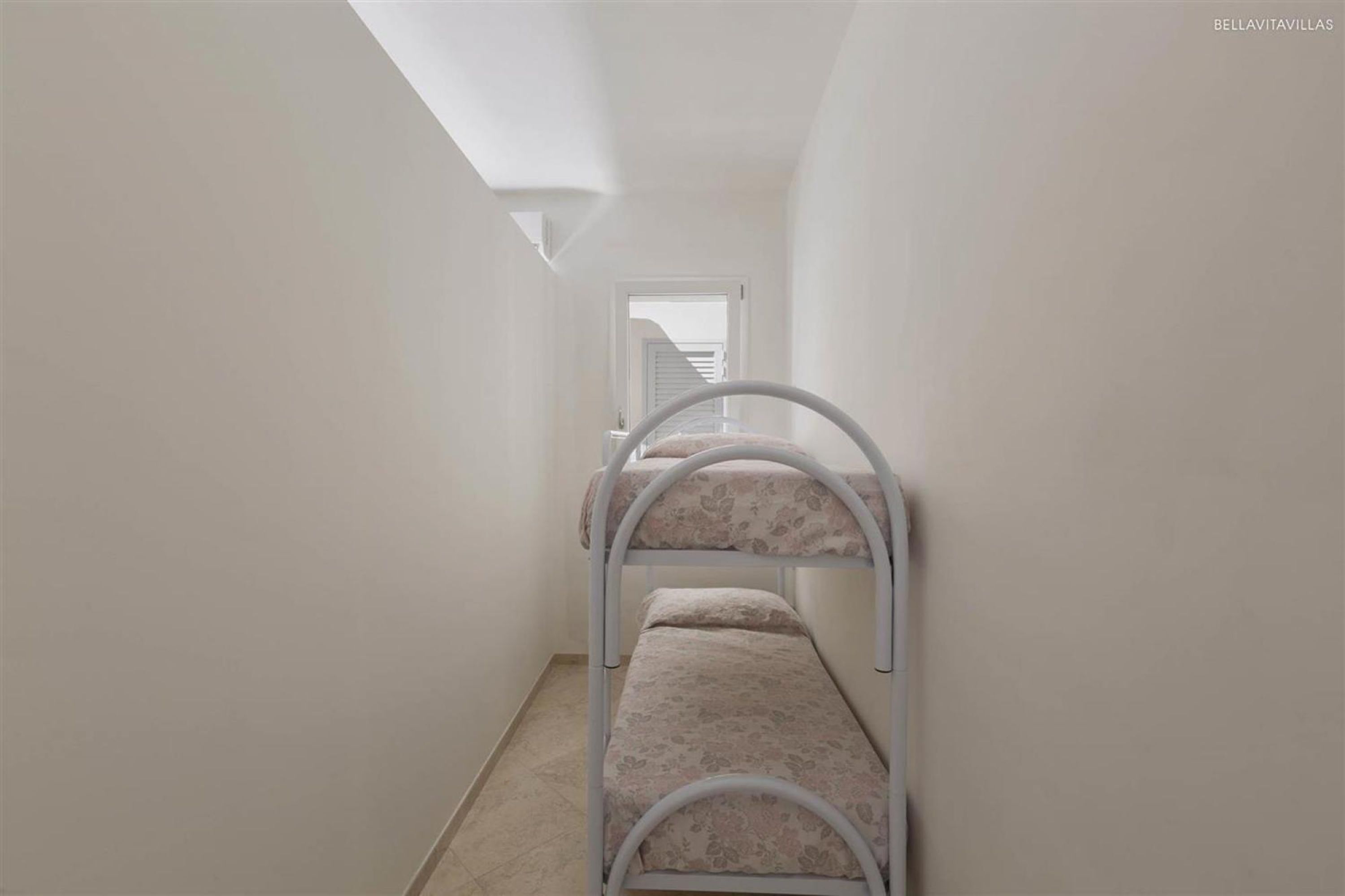 A narrow hallway with bunk beds, a staircase at the end, and a skylight above.