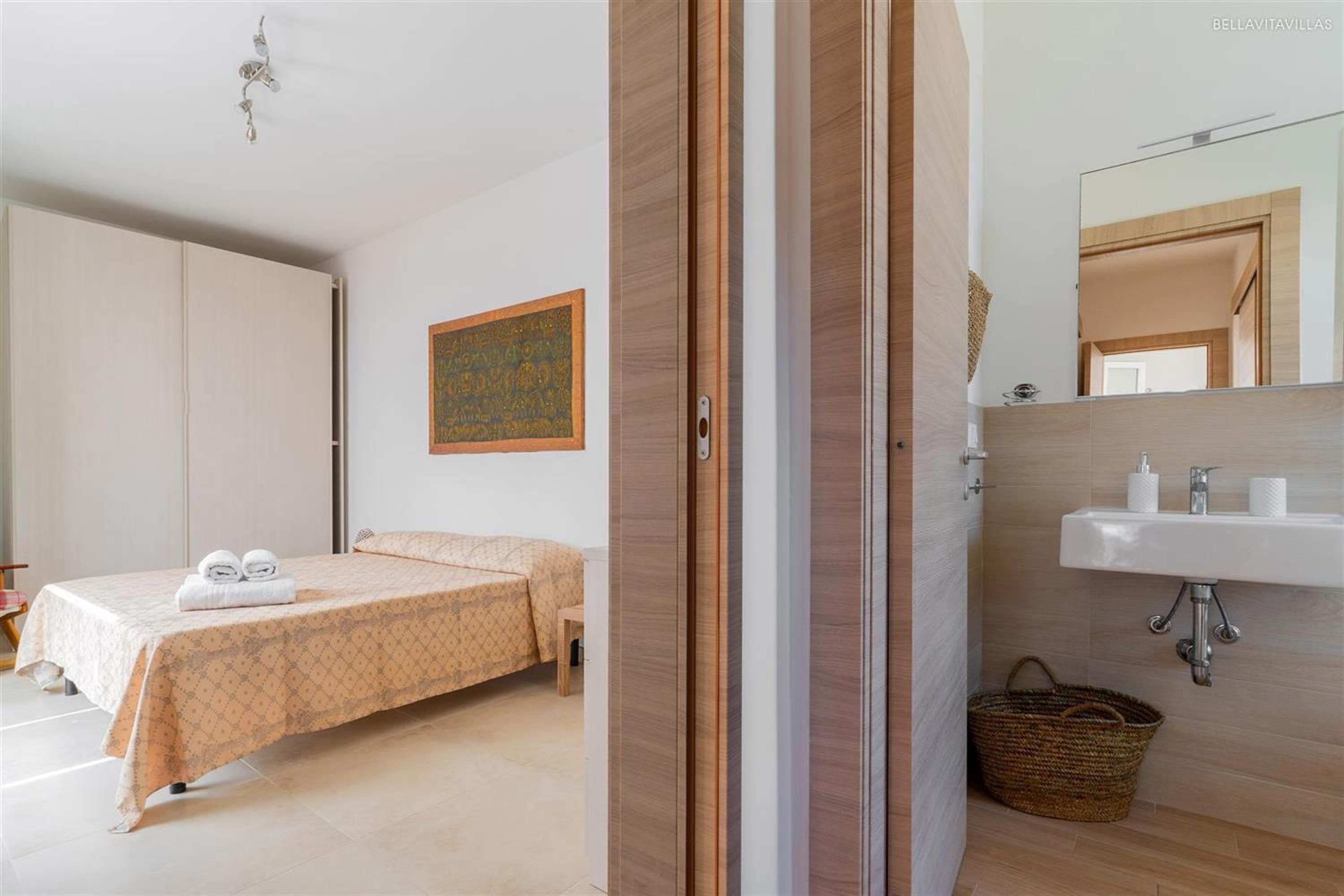 Une chambre d’hôtel comprenant un lit, une table de chevet, un miroir fixé au mur, un lavabo et une œuvre d’art accrochée au mur.