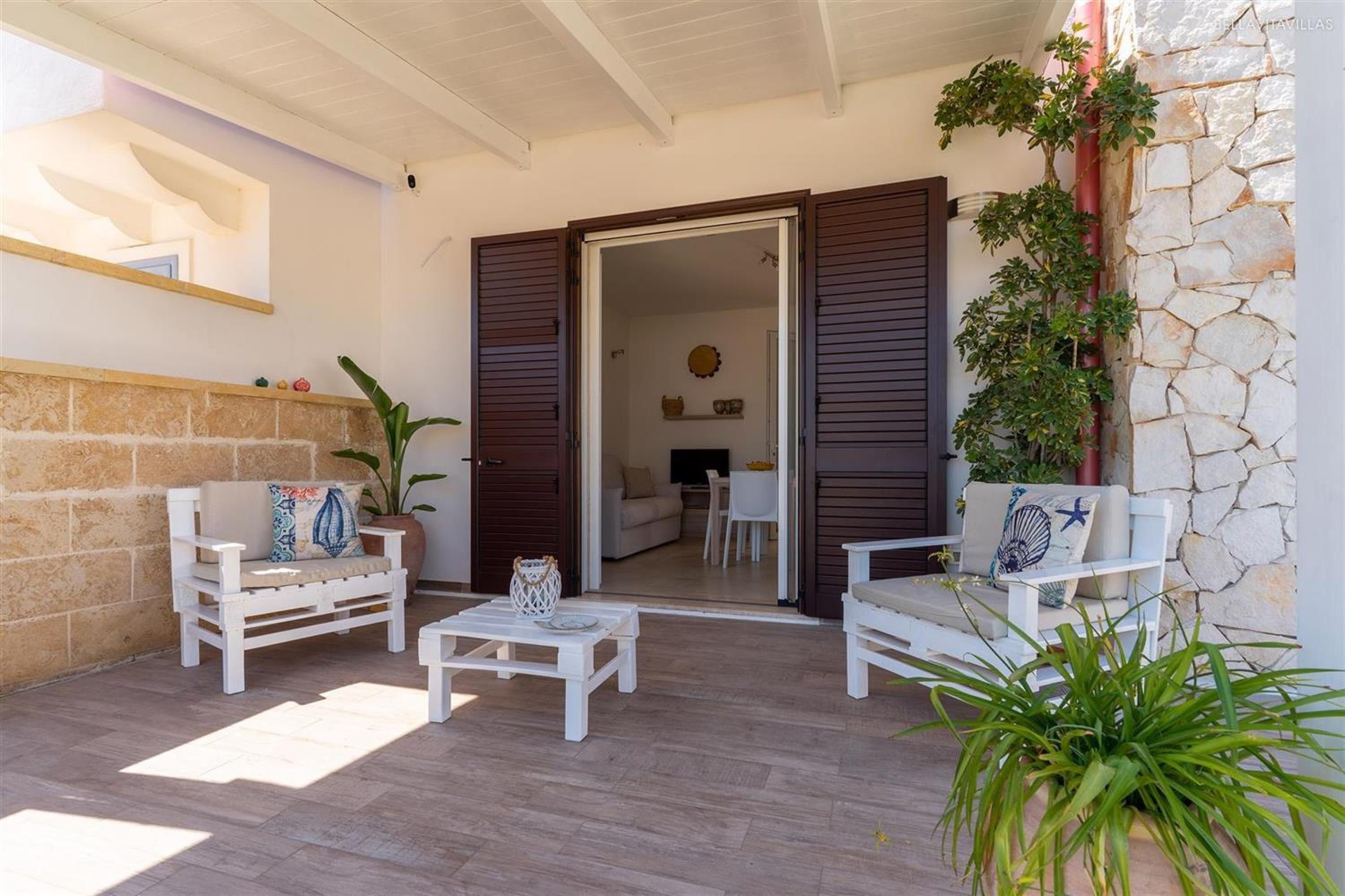 An outdoor seating area with white furniture, a stone wall, and potted plants.