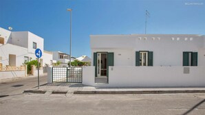 Un bâtiment moderne de couleur blanche, doté d’une entrée sécurisée par un portail, sous un ciel bleu dégagé, et un panneau de signalisation indiquant une direction à prendre à gauche.