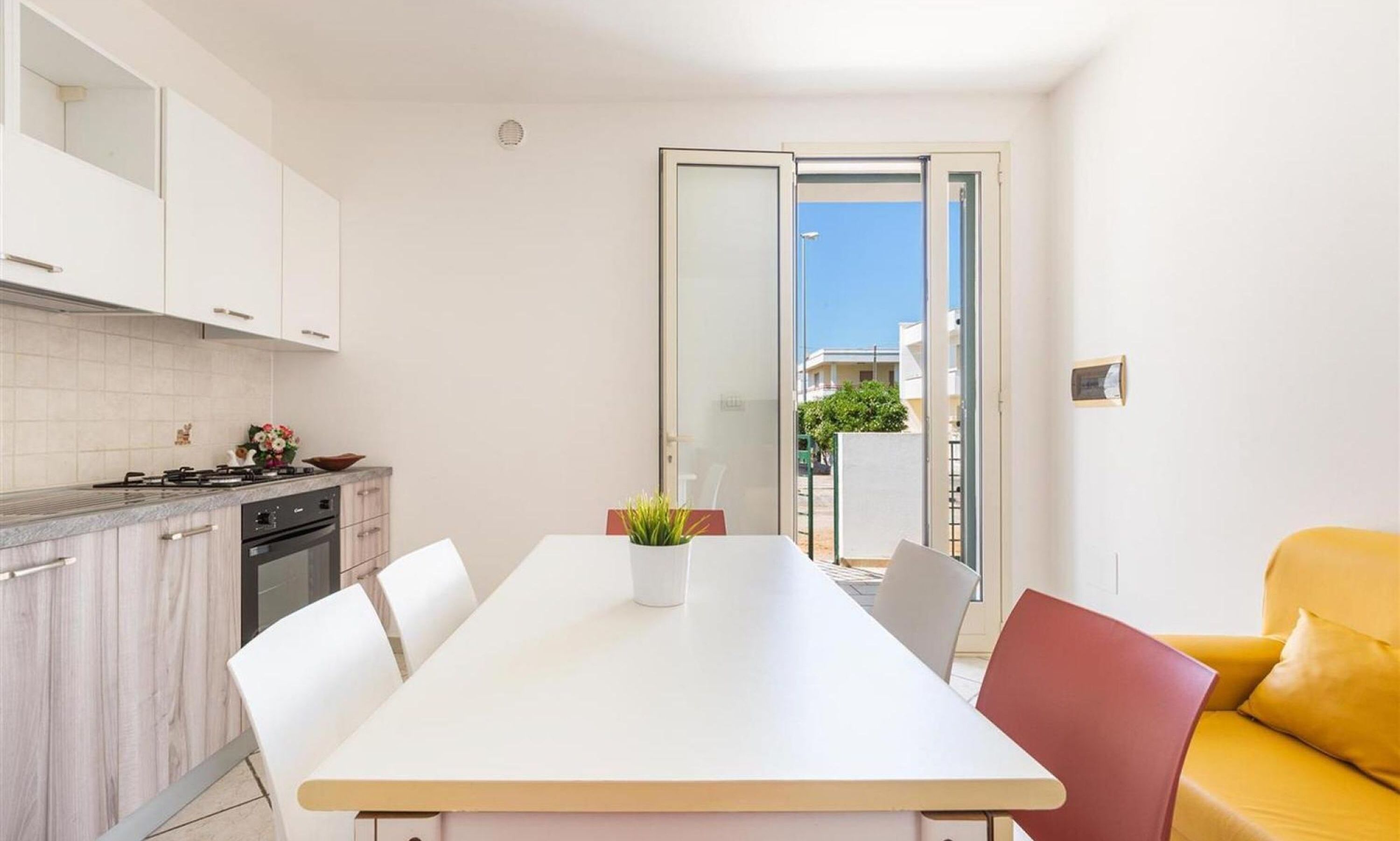 A compact kitchen with white cabinets, a stove, and a dining area with a white table and chairs.