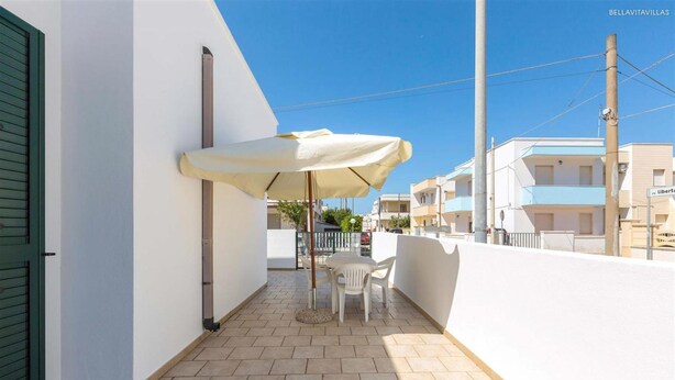 Un balcon avec un parasol blanc, une table et des chaises.