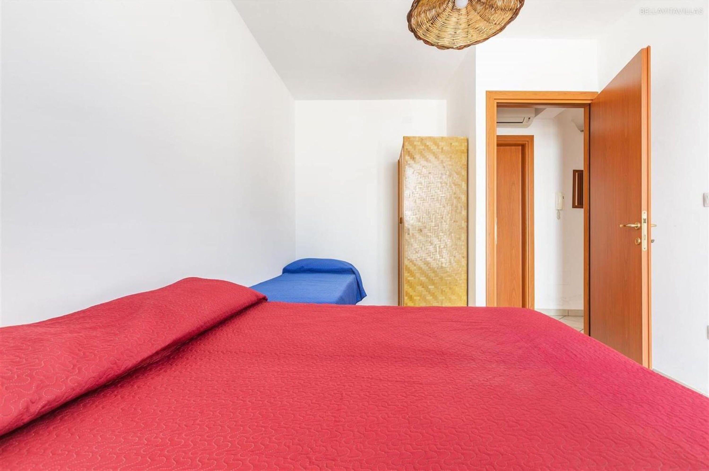 A bedroom with a bed, a blue chair, a wooden door, and a wall-mounted shelf.