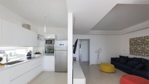 Una cocina moderna con armarios blancos, horno integrado y microondas. Hay un rincón de comedor con un sofá oscuro y otomanas coloridas.