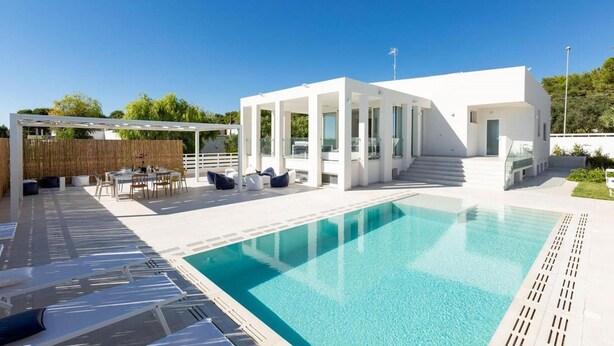 Un área de piscina moderna al aire libre con una zona de estar cubierta y una escalera que conduce a un segundo piso.