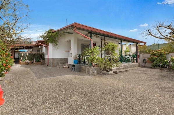 A two-story house with a covered porch, a gravel driveway, and potted plants.