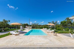 Une piscine rectangulaire, agrémentée de chaises longues et de parasols, entourée d’un jardin aménagé et d’une terrasse dallée.