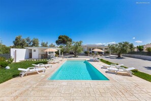 Une piscine avec des chaises longues, un espace de détente abrité et un ciel d’un bleu éclatant.