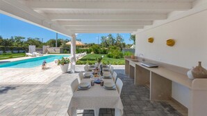 An outdoor dining area with a pool view, a pergola, and a kitchen counter. - 2390 Villa Eva by Perle di Puglia (San Vito dei Normanni)