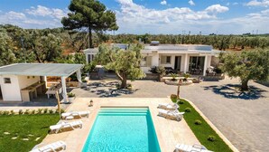 A swimming pool with lounge chairs, a covered patio, and a view of olive trees and a building. - 2390 Villa Eva by Perle di Puglia (San Vito dei Normanni)