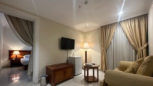 Et hotelværelse med en seng, fjernsyn, skrivebord, lampe, sofa og gardiner.