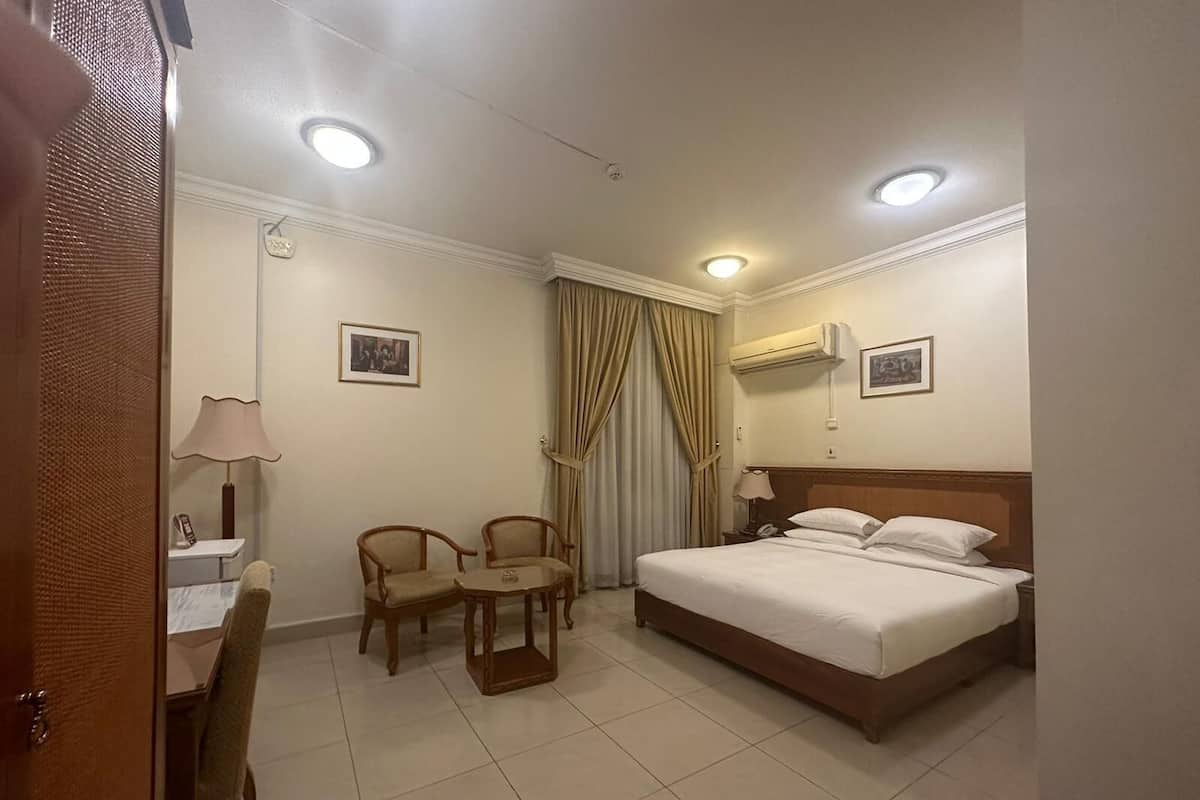 Habitació d'hotel amb un llit, dues cadires, un escriptori amb una làmpada i cortines.