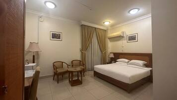 A hotel room with a bed, two chairs, a desk with a lamp, and curtains.